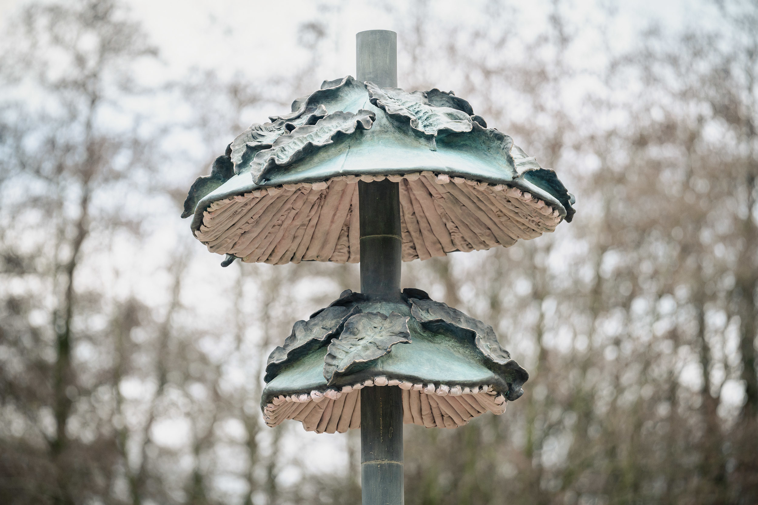 Twee geplooide elementen op een bamboestam. De groene buitenkant is bedekt met bladeren. De gegroefde binnenkant is geïnspireerd op die van paddenstoelen. Twee geplooide elementen op een bamboestam. De groene buitenkant is bedekt met bladeren. De gegroefde binnenkant is geïnspireerd op die van paddenstoelen.
